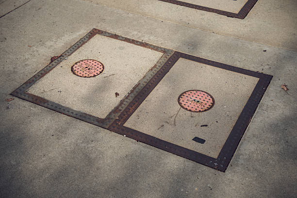 Close-up view of two weathered metal access covers with pink circular plates indicating 'WATER BUREAU' embedded in a concrete surface, suggesting urban infrastructure