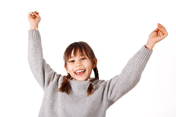 Happy young caucasian girl with long hair and arms raised celebrating success or joy. Kid posing for professional studio photoshoot on white background.