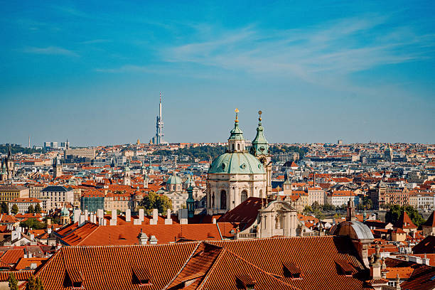 Prague Rooftops Featuring Baroque Dome Under Blue Sky. Sunlit Terracotta Tiles Cascade Toward Historic Spires,