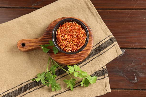Saffron in bowl and coriander on wooden table, flat lay. Aromatic spices