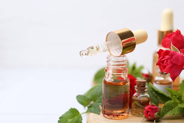 Bottles of essential oils, red roses and herbs on table, closeup. Space for text