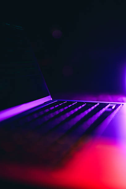 Laptop keyboard under dramatic purple and red neon lighting in a dark room