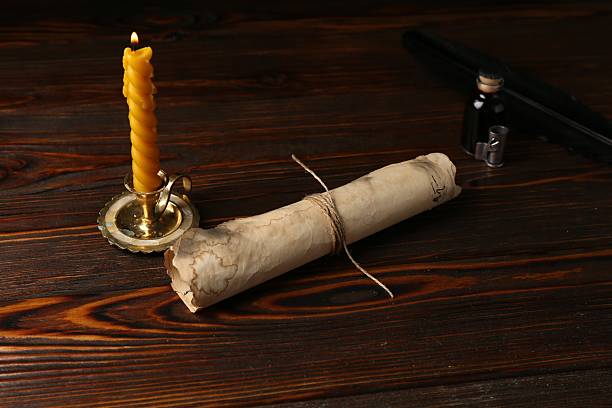 Old paper scroll, feather, inkwell and burning candle on wooden table, closeup
