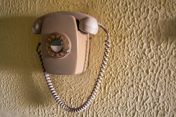 Retro beige rotary telephone mounted on a textured yellow wall. The nostalgic aesthetic and color contrast evoke classic communication, vintage design and retro interior decoration.