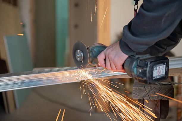 Close-up of a professional worker using an electric angle grinder to cut a steel stud for drywall installation, visible bright sparks.