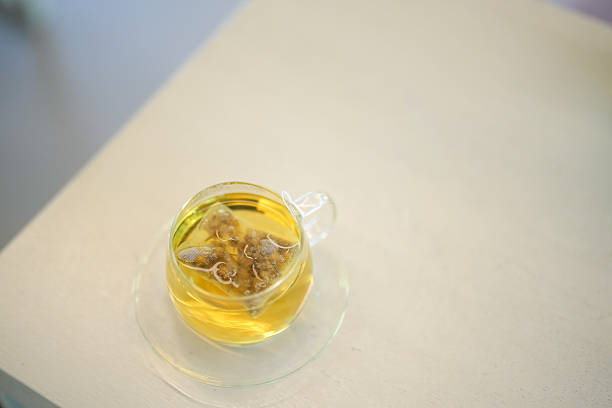 A cup of tea with a small amount of herbs in it. The cup is sitting on a white table