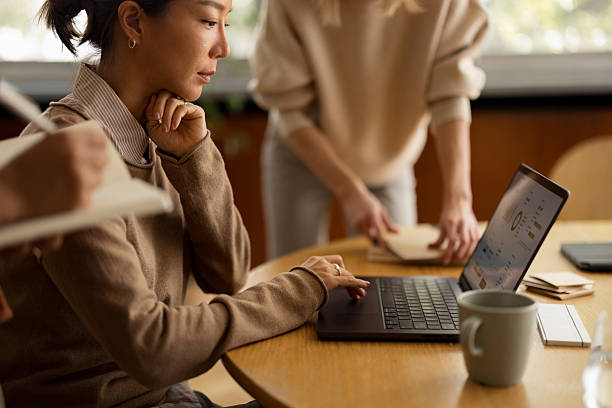 Focused colleague working on laptop, analyzing data during a business meeting with coworkers collaborating and taking notes