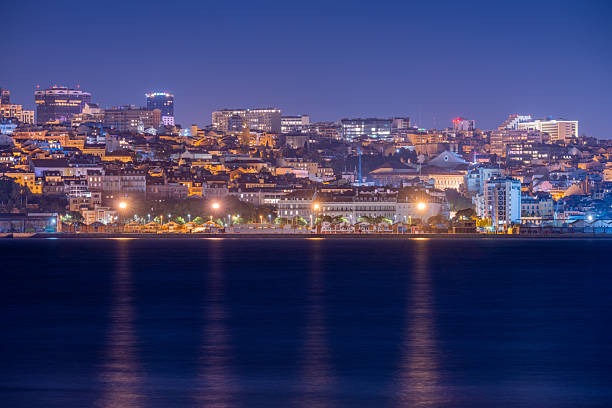 Lisbon Portugal December 24 2025. Dense urban skyline lines the Tagus River with warm city lights reflecting across calm water at night.