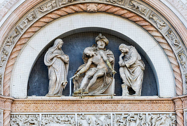 A group of three sculpted marble figures is displayed in a semi-circular niche on a historic building facade, enclosed by protective netting.