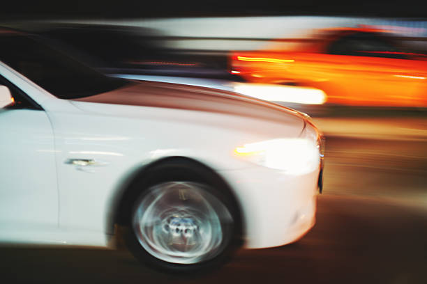 A generic electric sports car moving at high speed around a corner of a slightly wet racetrack in rear view with brake lights on. Under a clear dusk/dawn sky with lots of motion blur to track foreground and wheels.
