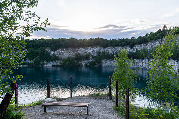 A wide view of Zakrzowek quarry lake with limestone cliffs, green trees, and calm blue water near Krakow. The image shows a popular natural swimming and recreation area surrounded by dramatic rock formations.