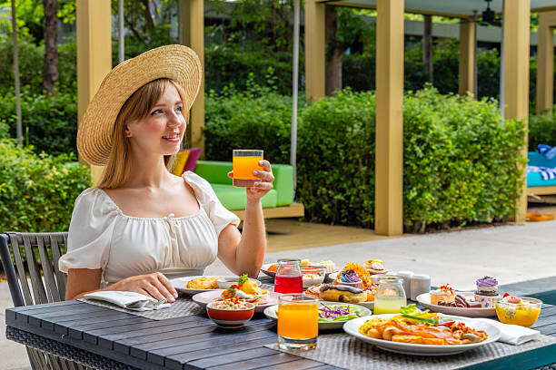 Woman enjoying brunch outdoors, wearing straw hat, holding orange