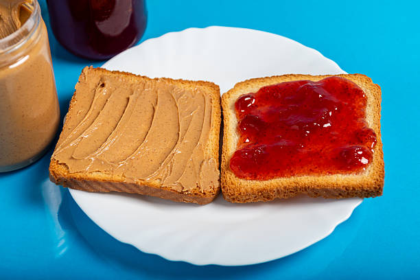 A peanut butter and jelly sandwich cut in half, on a white plate against a bright blue background.