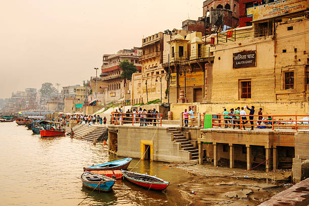 Vibrant riverside scene in Varanasi, India, showing boats along the Ganges, ancient ghats, and crowds along the embankment. Warm sunset light enhances the sense of daily life, culture, and travel by the river.