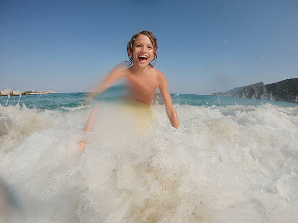 Young caucasian boy jumping into waves. He is swimming and diving in clear turquoise colored sea.
