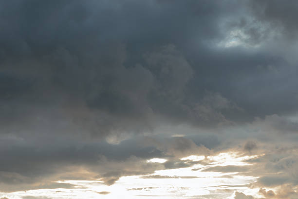 Sky is filled with dark, turbulent storm clouds, signaling approaching bad weather. Bright sunlight breaks through the bottom edge, providing a sharp contrast