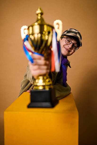 Young boy smiling proudly while holding a shiny golden trophy with ribbons