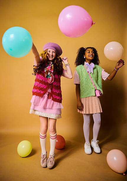 Two diverse elementary school girls jumping, playing with balloons, symbolizing fun and friendship