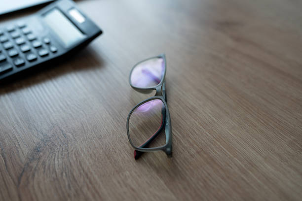 Eyeglasses resting on a wooden desk with a calculator in the background