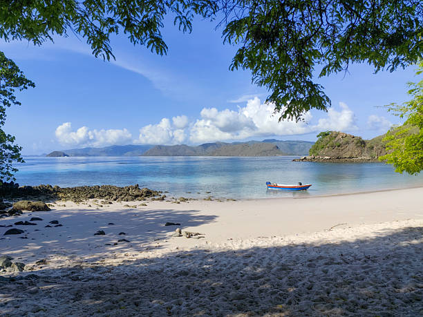 Quiet tropical beach with a small boat anchored near the shore in Komodo National Park, Indonesia.