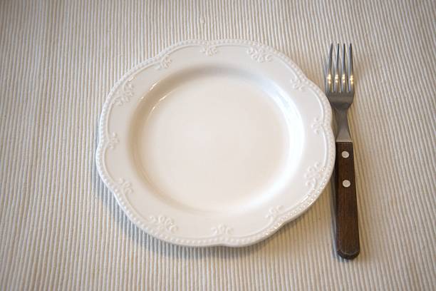 A white plate with texture or irregularities, angled and off-center on a light grey background Soft, diffused lighting implies ambient source Minimalist composition with no texts or other objects