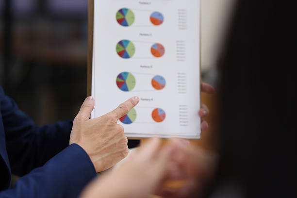 Business professional holding and pointing at a document with pie charts showing financial data during an office meeting
