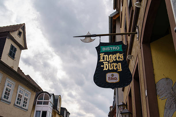 Aschaffenburg, Bavaria, Germany - August 30, 2025: Decorative hanging sign displayed above café in traditional half-timbered house against the cloudy sky. Historic German craftsmanship, the sign symbolizing the character and name of the establishment.