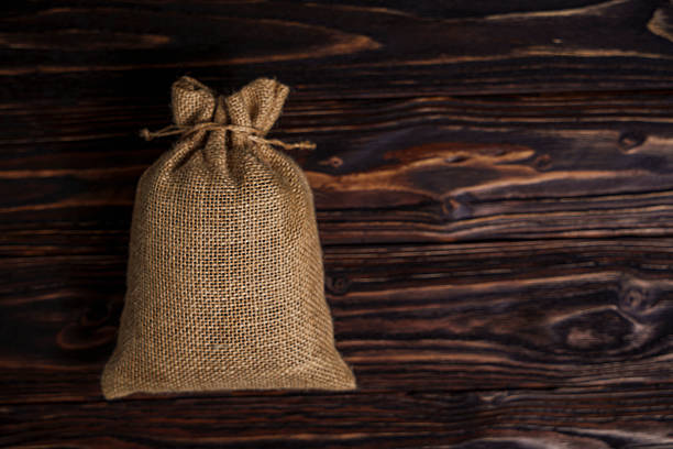 A tied burlap sack sits on a dark wooden surface with rich texture and copy space, evoking rustic and natural themes