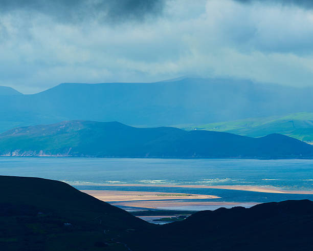 View of Castlemaine Harbour from a mountain vantage point on a cloudy day, showing distant hills and tidal flats.