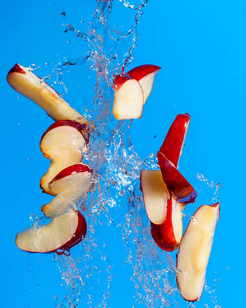 Apple slices splashing in water against bright blue background