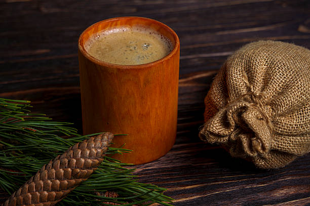 A rustic ceramic coffee cup sits beside a pine cone, burlap sack, and evergreen sprig on a dark wooden table in a cozy, forest-inspired still life scene