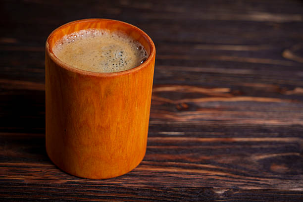 A foamy cup of coffee sits on a dark wooden table, viewed from above, creating a warm and rustic morning atmosphere