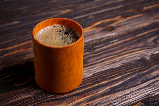A foamy cup of coffee sits on a dark wooden table, viewed from above, creating a warm and rustic morning atmosphere