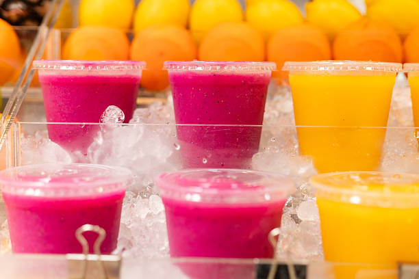 Several cups filled with vibrant fruit drinks sit on a layer of ice. Bright orange cups are positioned behind deep pink cups, signaling the flavors available.