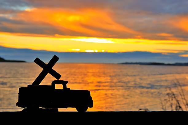 Cross on back of a pickup truck with a wonderful sunset over a bay of water.