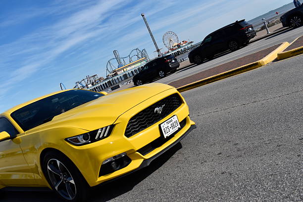 Galveston, TX USA January 11, 2026 - A yellow Ford Mustang graciously cruising on Seawell Blvd. The coastline and amusement park (Pleasure Pier) gives this image its dominant marketing appeal.