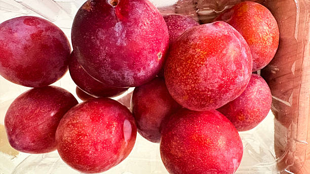 A close-up view of fresh red plums in a clear plastic bag