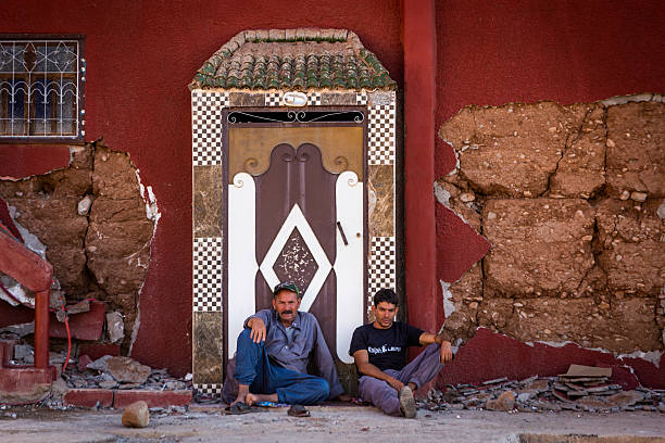 Marrakesh, Morocco – September 22, 2023: Men sit and lean against a wall damaged by the 2023 earthquake in Morocco, days after the disaster.