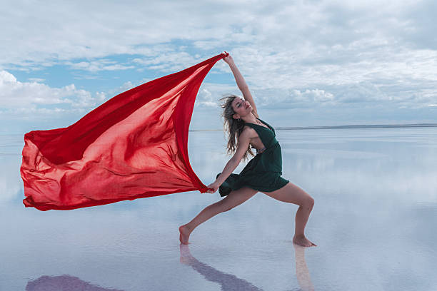 Person in red skirt and striped shirt dances joyfully on reflective surface surrounded by big landscape of mountains, moving forward with hope for future