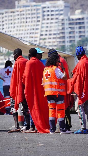 Port of Arguineguín, Las Palmas, Canary Islands, Spain - August 28, 2024 - Red Cross workers assisting migrants with blankets and support after arrival in Gran Canaria