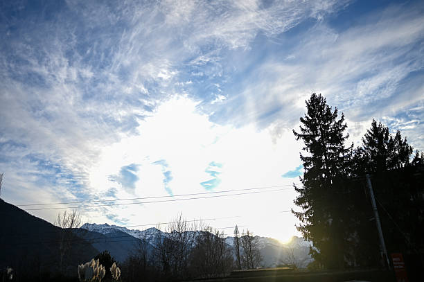 Sun flare illuminating cirrus clouds over distant snowy hills and pine trees