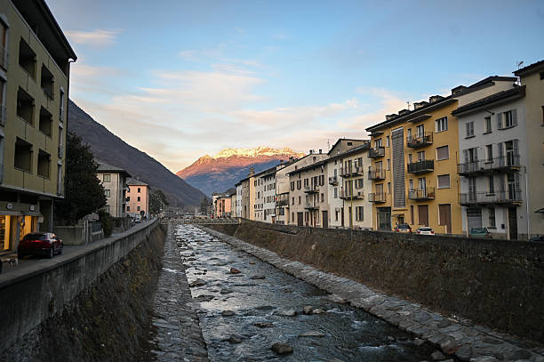 River Mallero flowing through the alpine town of Sondrio with buildings and snow-capped mountains