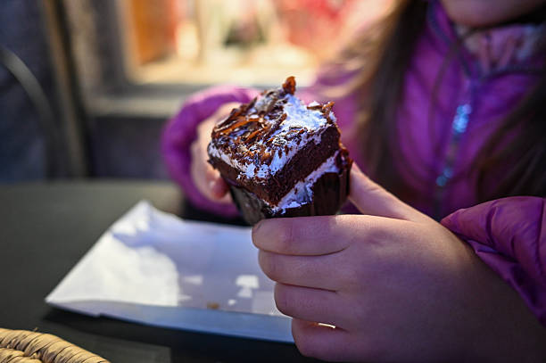 Young child enjoying a sweet dessert, holding a chocolate cake with whipped cream