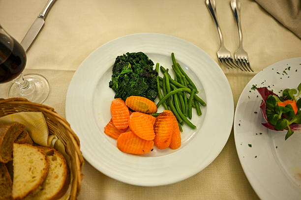 Assortment of healthy cooked vegetables as a side dish, served with bread and wine at a restaurant table