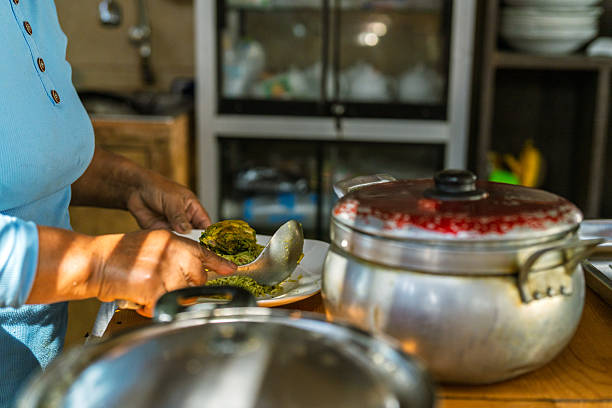 Person serving hot food onto a plate using a spoon in a rustic kitchen environment, preparing a home-cooked meal
