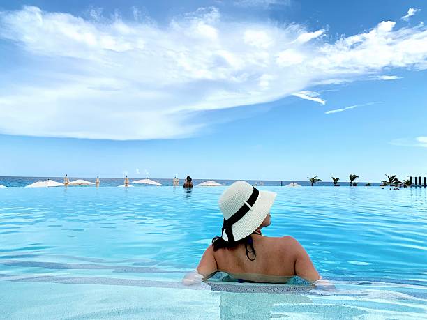 A woman in Cancun, Mexico soaks up the sun while sitting in an infinity pool under a partially clouded sky.