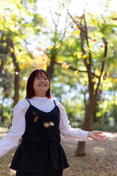 Happy woman throwing up fallen leaves in forest