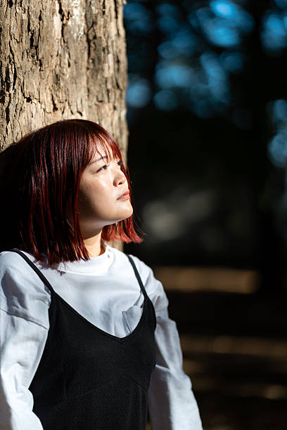 Woman leaning on tree in forest - light and shadow