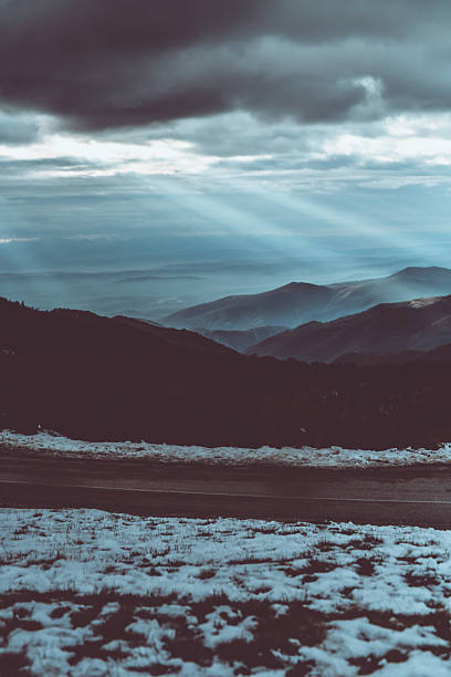 A tranquil snowy mountain scene featuring distant ridges, soft sun rays breaking through clouds, and a quiet, expansive valley below. Perfect for nature, travel, and winter mood visuals.