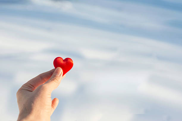 Close-Up Of Hand Holding Heart Shape Against Blue Sky